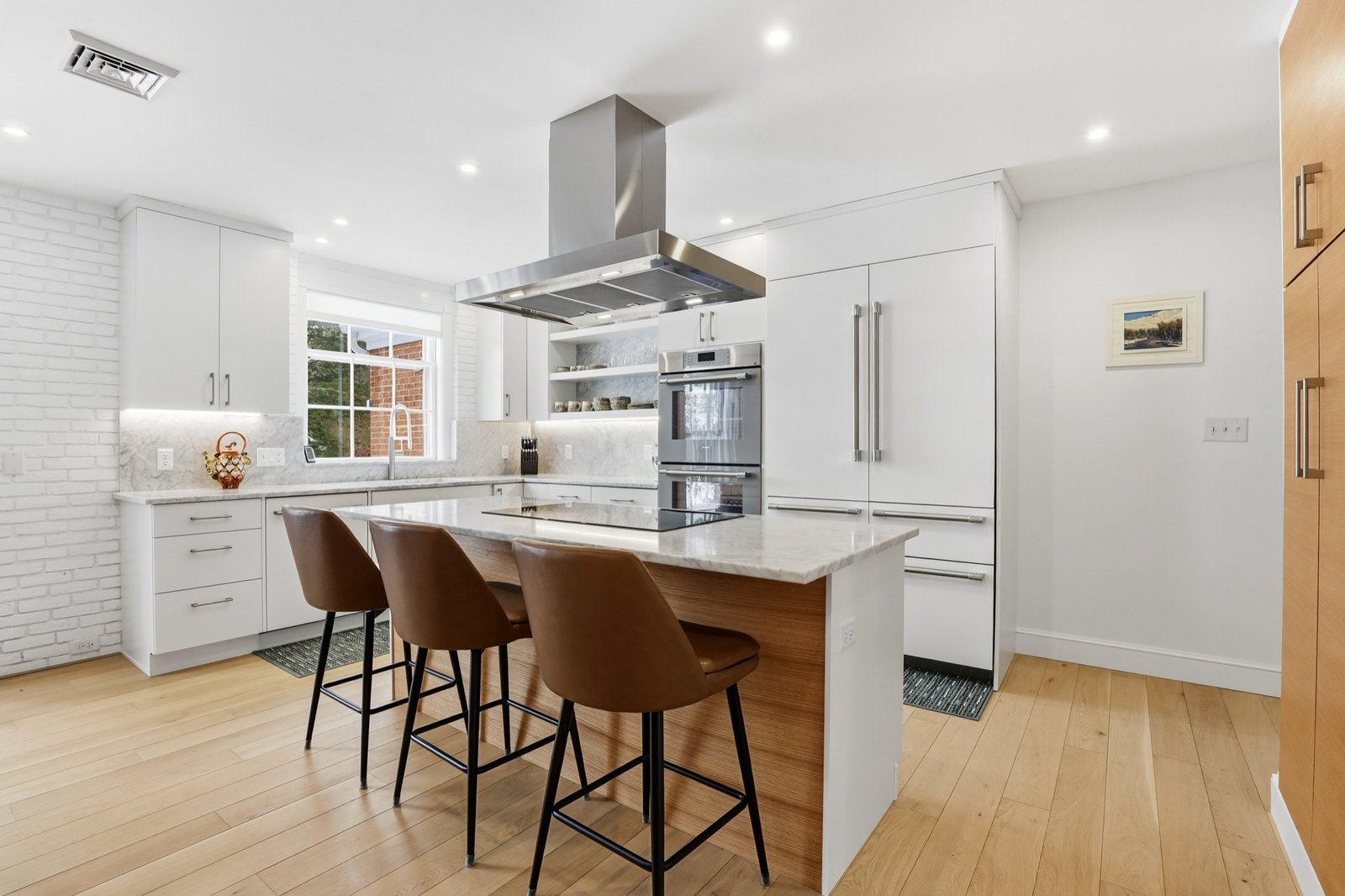 Bright white kitchen with marble island, leather stools, and light oak floors