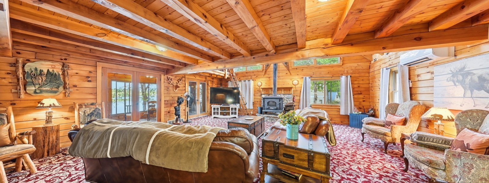Panoramic view of a log cabin great room with exposed beams and a woodstove