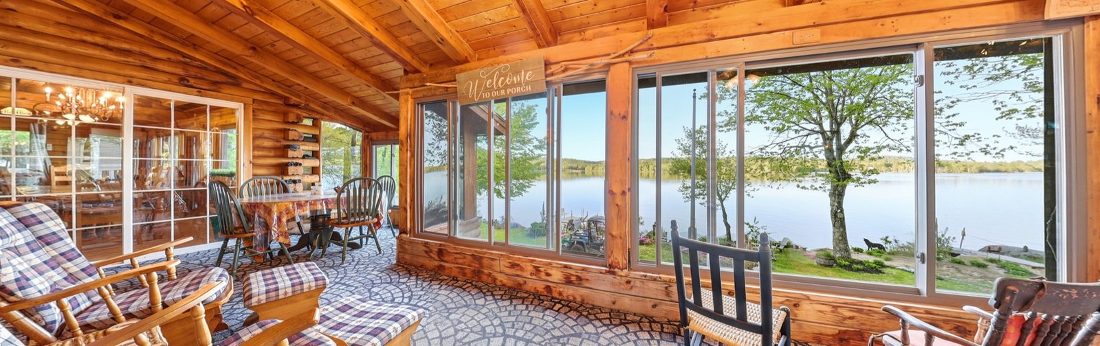 Panoramic view of a log cabin screened porch with lake views and wicker rocking chairs