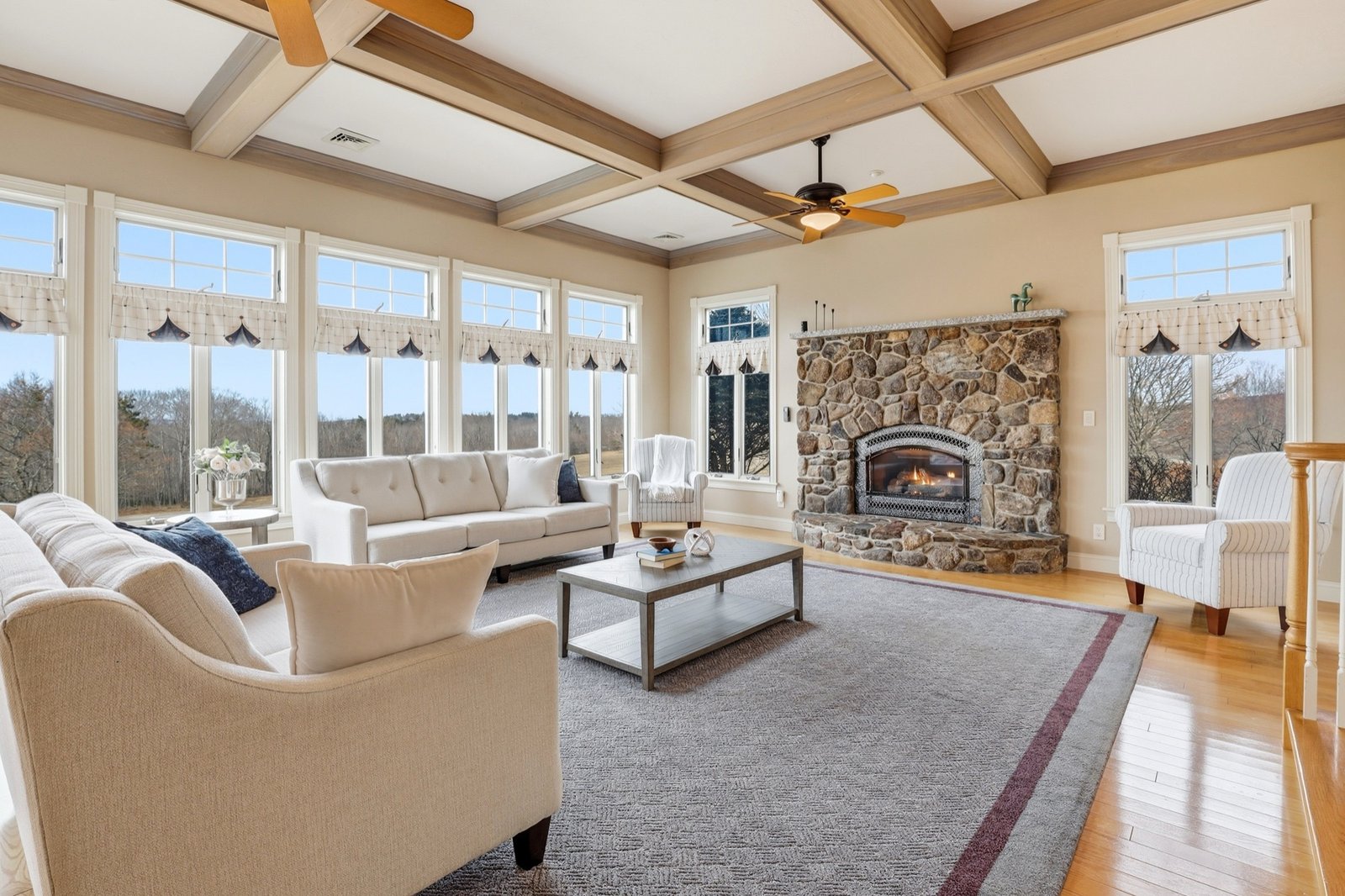 Great room with coffered ceiling, stone fireplace, and wall of windows
